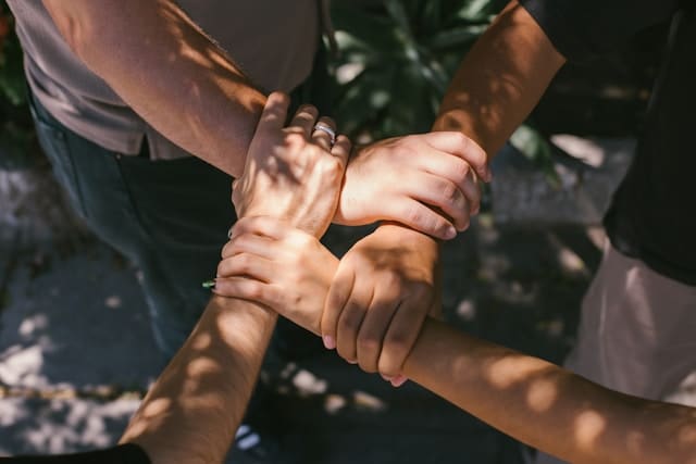 four hands of different people holding each other in support.