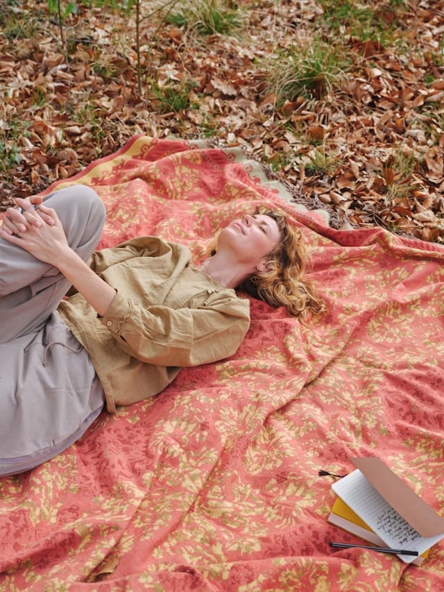woman relaxing on a plaid in nature with closed eyes, her diary on the side