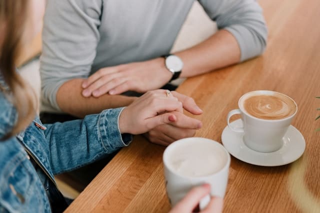 a man and a woman holding hands while having a conversation over coffee