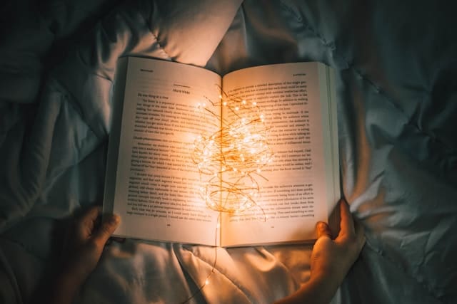 Open book with little lights on it on a cozy bed