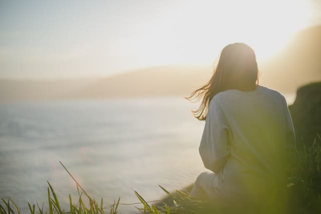 a woman sitting quietly by the water, reflecting on how to accept yourself