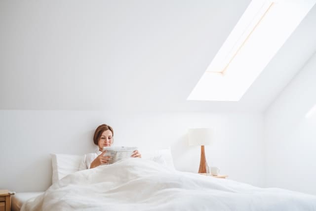 be kind to yourself — a woman reading in bed in the morning, unhurried, in soft light